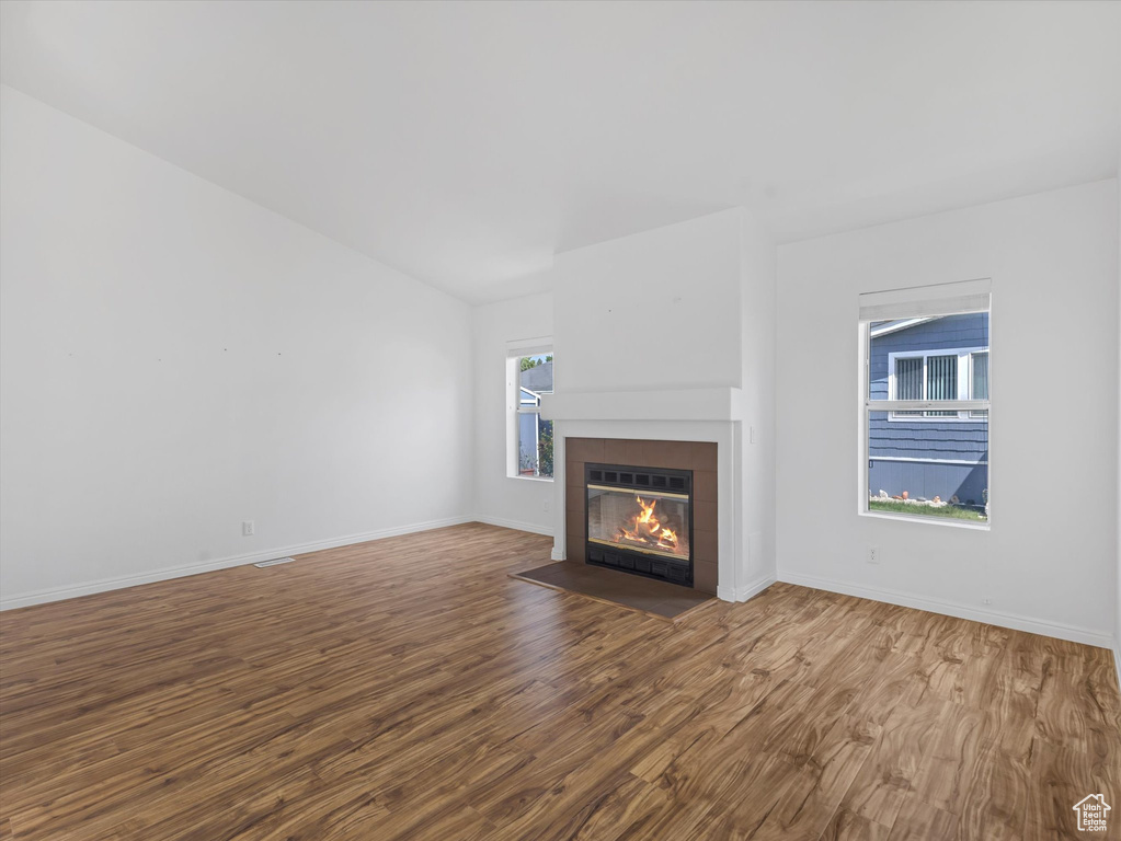 Unfurnished living room with wood finished floors, a fireplace with flush hearth, and baseboards