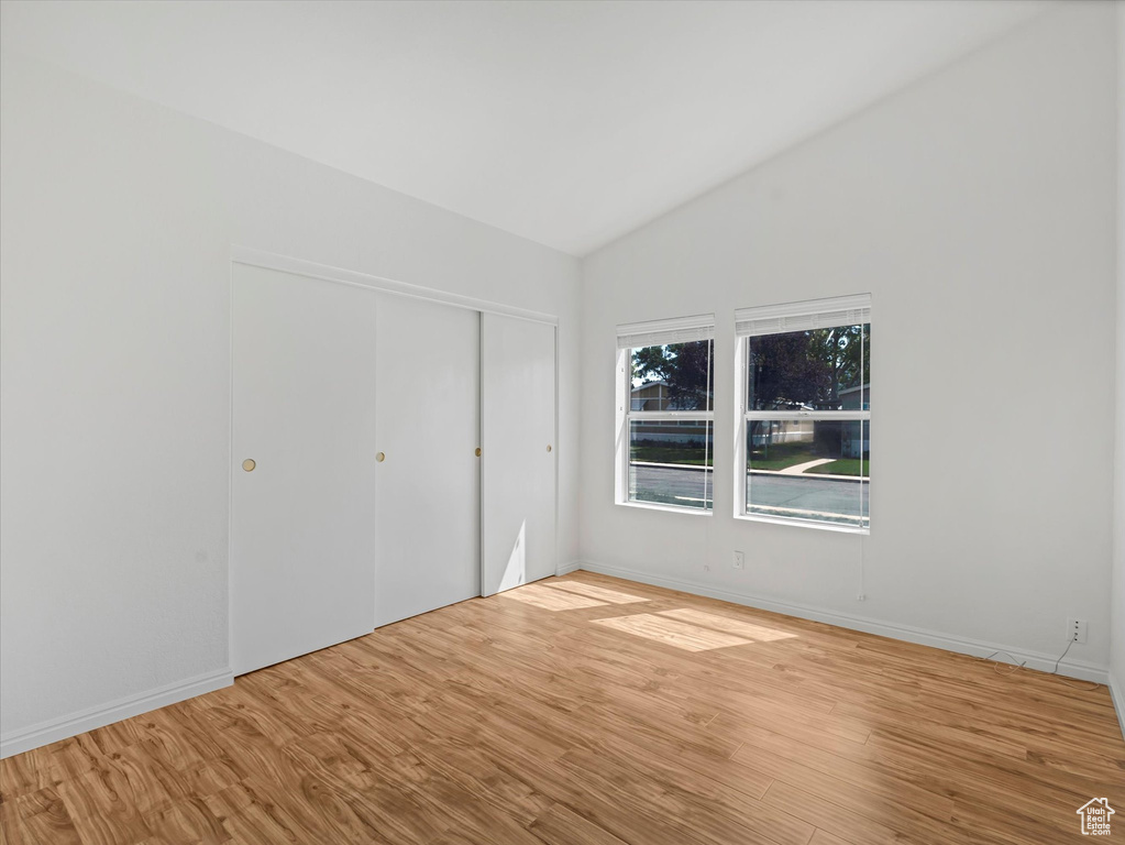 Unfurnished bedroom with lofted ceiling, wood finished floors, baseboards, and a closet