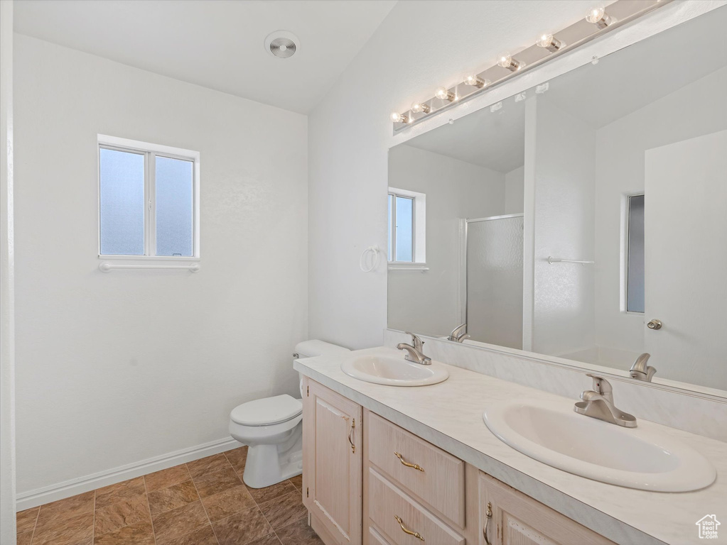 Bathroom featuring baseboards, double vanity, a shower with door, and toilet