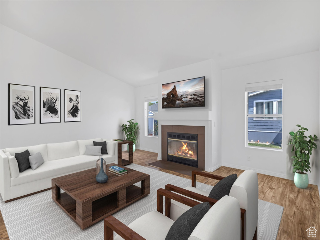 Living area featuring a fireplace with flush hearth, light wood finished floors, baseboards, and lofted ceiling