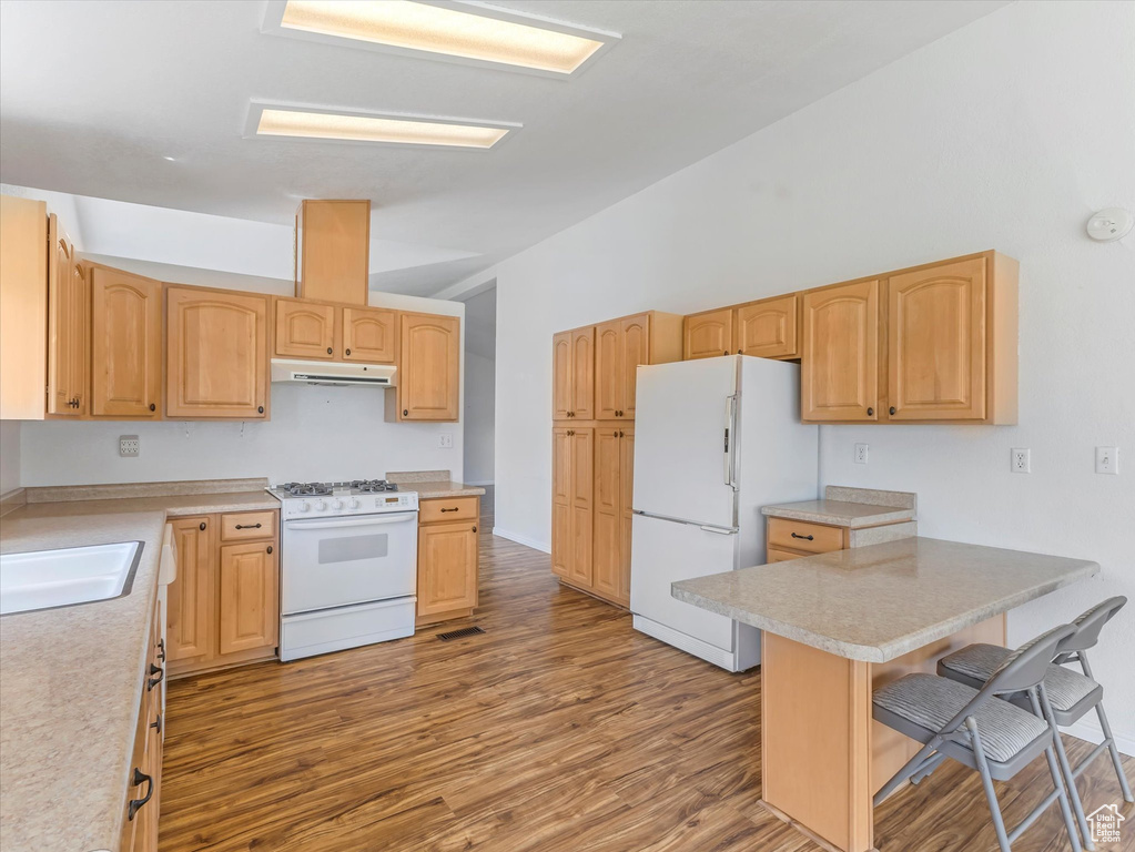 Kitchen with white appliances, under cabinet range hood, a breakfast bar, wood finished floors, and light countertops