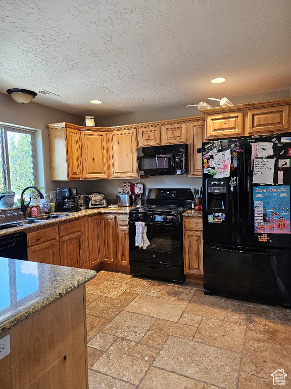Kitchen featuring black appliances, a textured ceiling, recessed lighting, light stone counters, and a sink