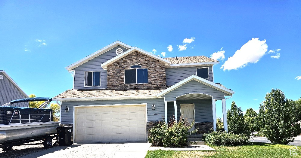 Traditional-style home featuring stone siding, an attached garage, and driveway