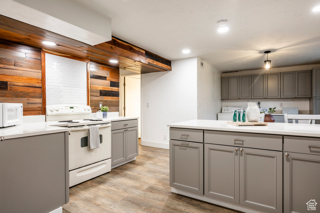 Kitchen featuring gray cabinetry, white appliances, wood walls, light wood-style floors, and light countertops