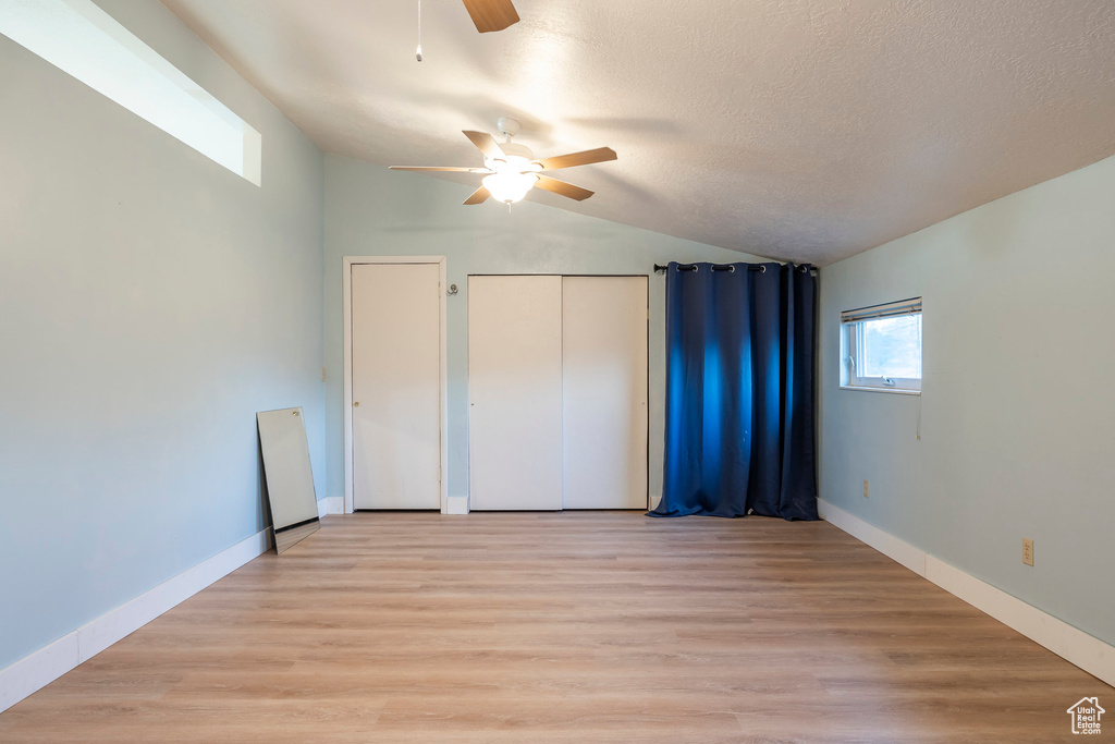 Unfurnished bedroom with lofted ceiling, light wood-style floors, ceiling fan, baseboards, and a textured ceiling
