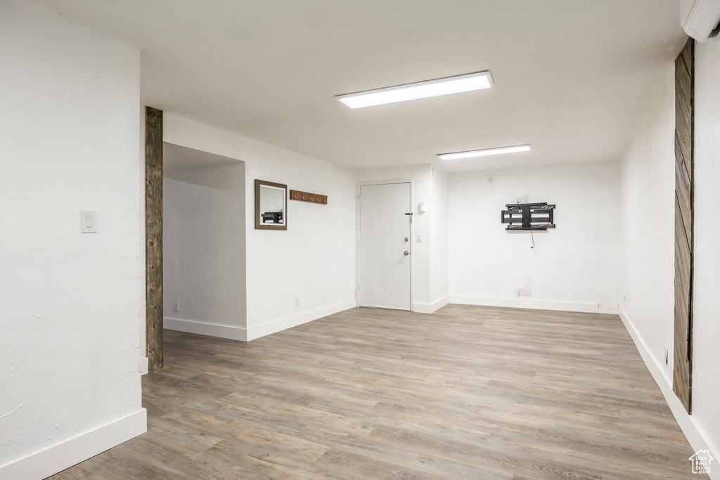 Empty room with an AC wall unit, light wood-type flooring, and baseboards