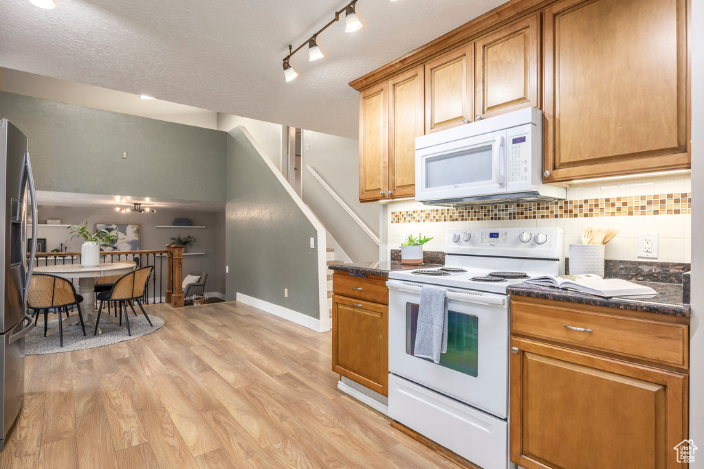 Kitchen featuring white appliances, backsplash, brown cabinets, light wood-style floors, and a textured ceiling