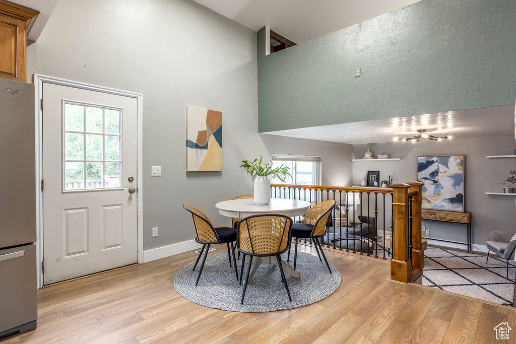 Dining room with light wood-type flooring, a towering ceiling, and baseboards