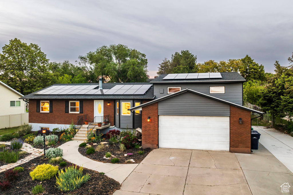 View of front facade with brick siding, solar panels, a garage, and driveway