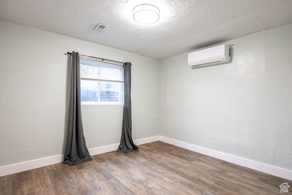 Empty room featuring a wall unit AC, wood finished floors, a textured ceiling, and baseboards