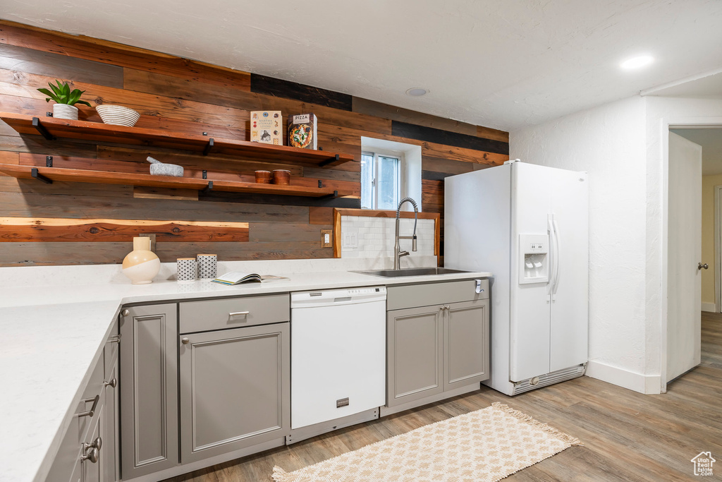 Kitchen featuring white appliances, gray cabinetry, wooden walls, and a sink