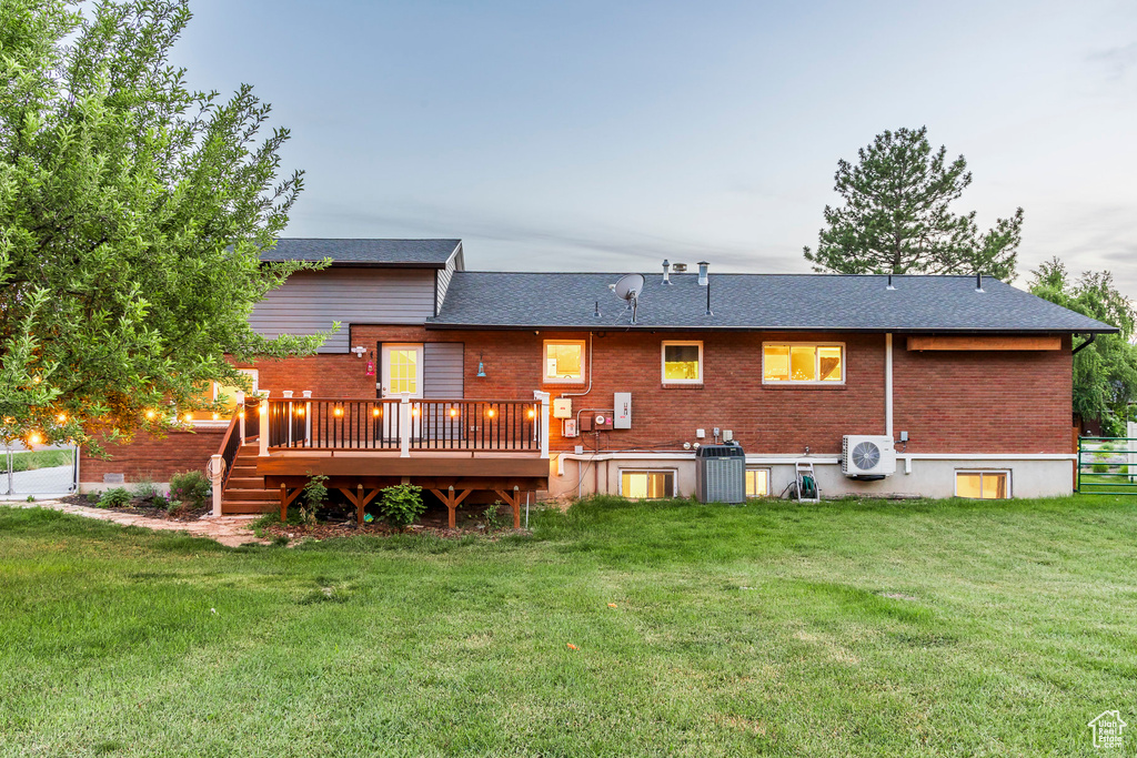 Back of property featuring brick siding, a wooden deck, ac unit, central AC, and a yard