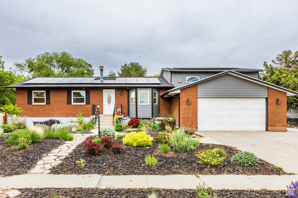 View of front of home featuring brick siding, an attached garage, solar panels, and driveway