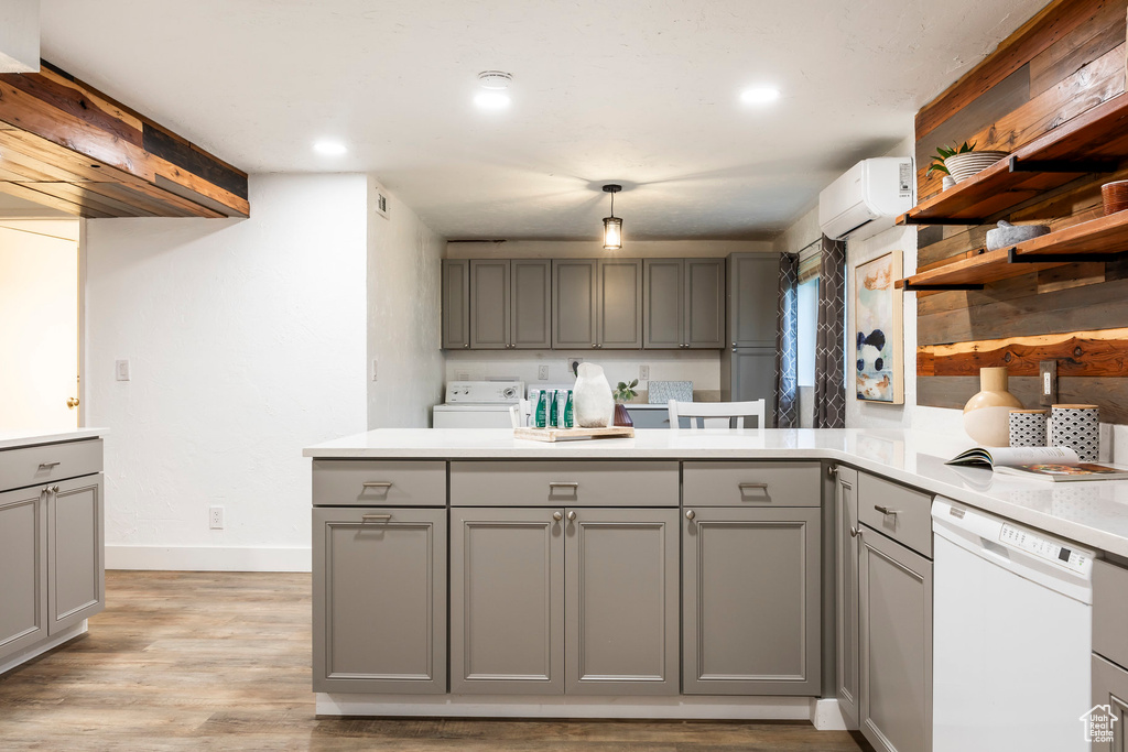 Kitchen featuring gray cabinetry, white dishwasher, a peninsula, baseboards, and washer and clothes dryer
