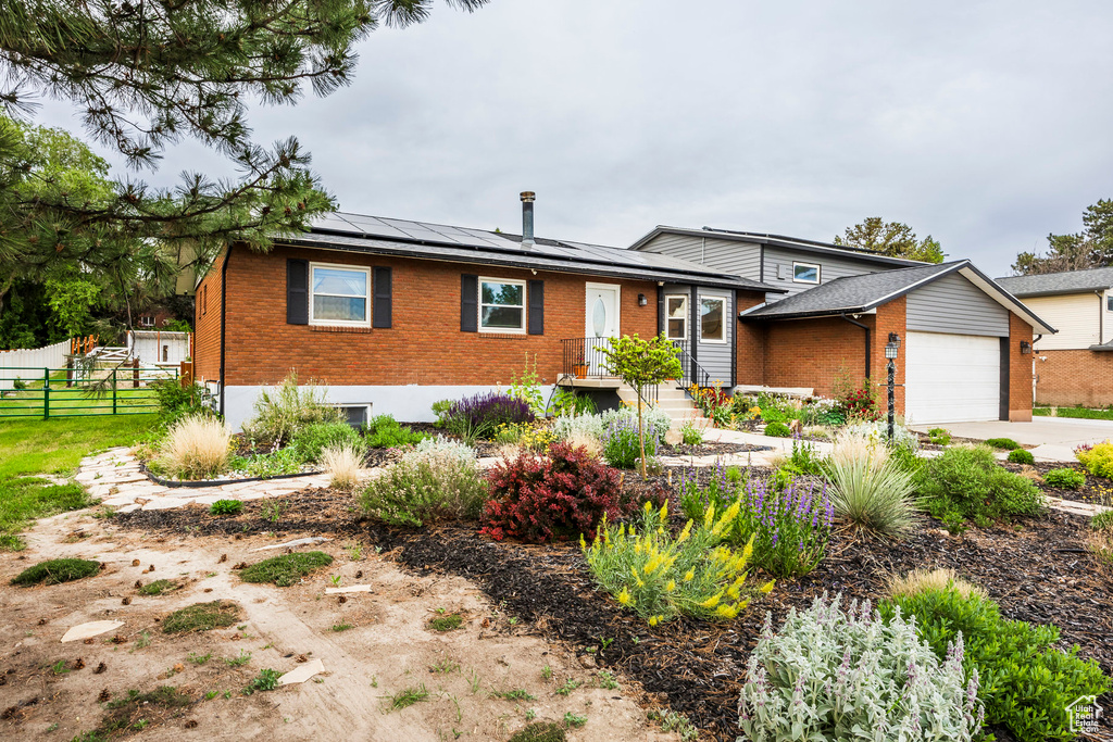 Tri-level home with brick siding, solar panels, an attached garage, and driveway