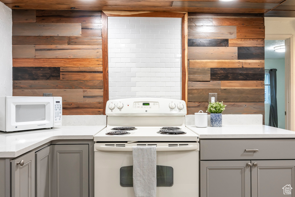 Kitchen with white appliances, gray cabinetry, wooden walls, and light countertops