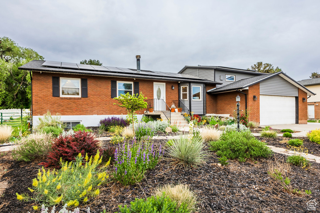 View of front of property with brick siding, a garage, and roof mounted solar panels