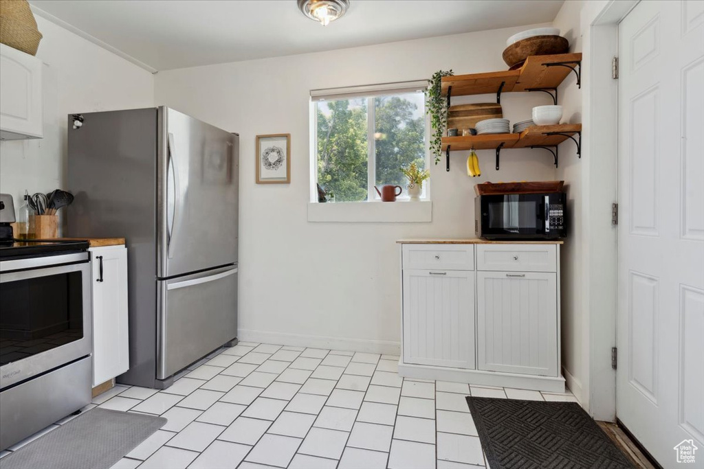 Kitchen with stainless steel appliances, white cabinetry, open shelves, and baseboards
