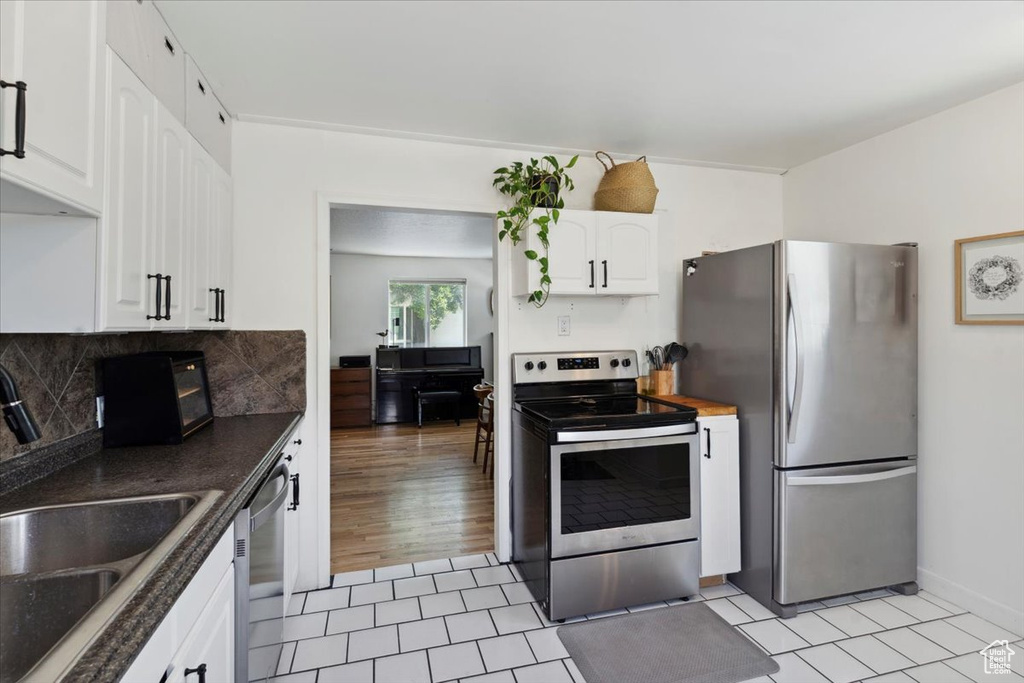 Kitchen featuring appliances with stainless steel finishes, a sink, white cabinetry, dark countertops, and backsplash