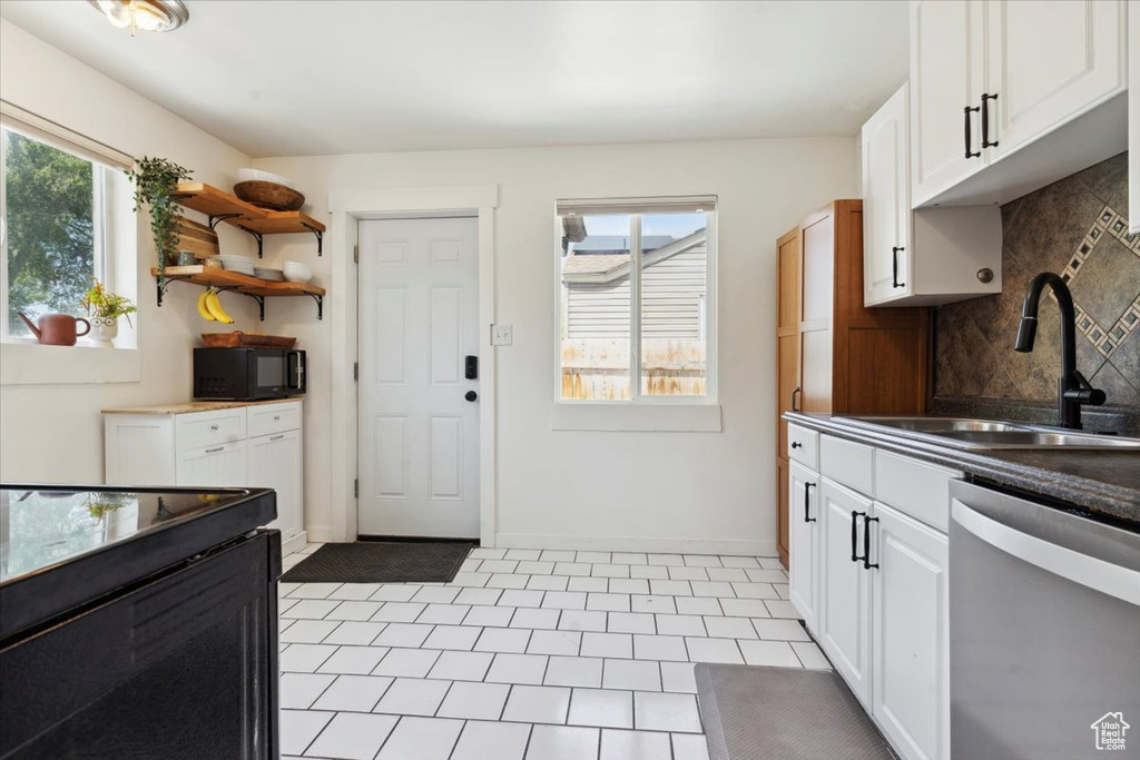 Kitchen featuring dishwasher, black microwave, a sink, tasteful backsplash, and white cabinets