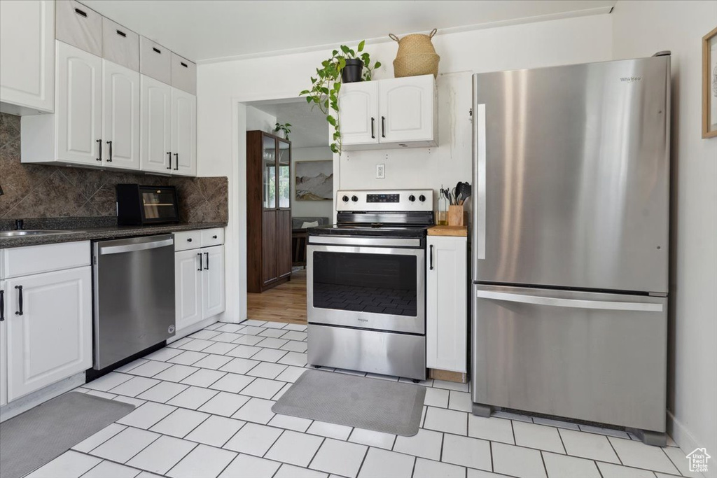 Kitchen with appliances with stainless steel finishes, white cabinetry, decorative backsplash, and a sink
