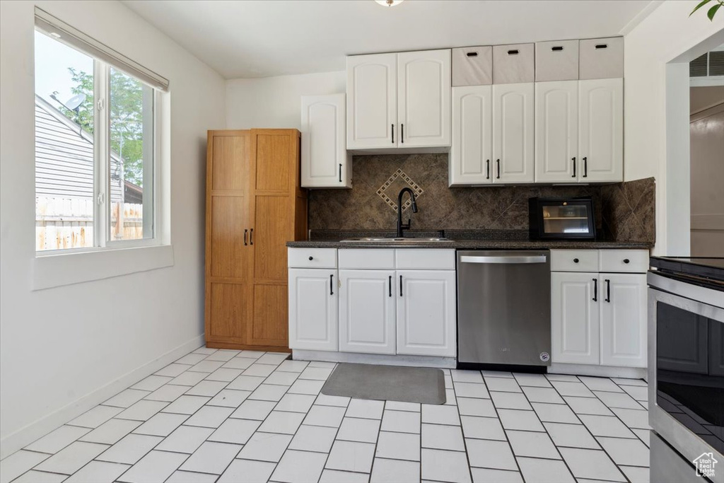 Kitchen featuring appliances with stainless steel finishes, a sink, backsplash, white cabinets, and baseboards