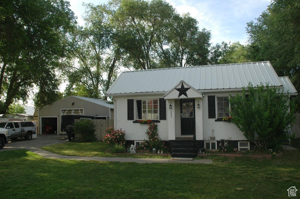 View of front of property with a detached garage, metal roof, a front yard, and an outdoor structure