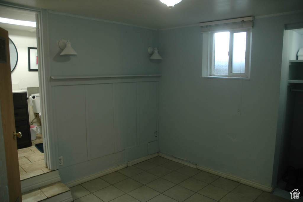 Unfurnished bedroom with a decorative wall, ornamental molding, wainscoting, and light tile patterned floors