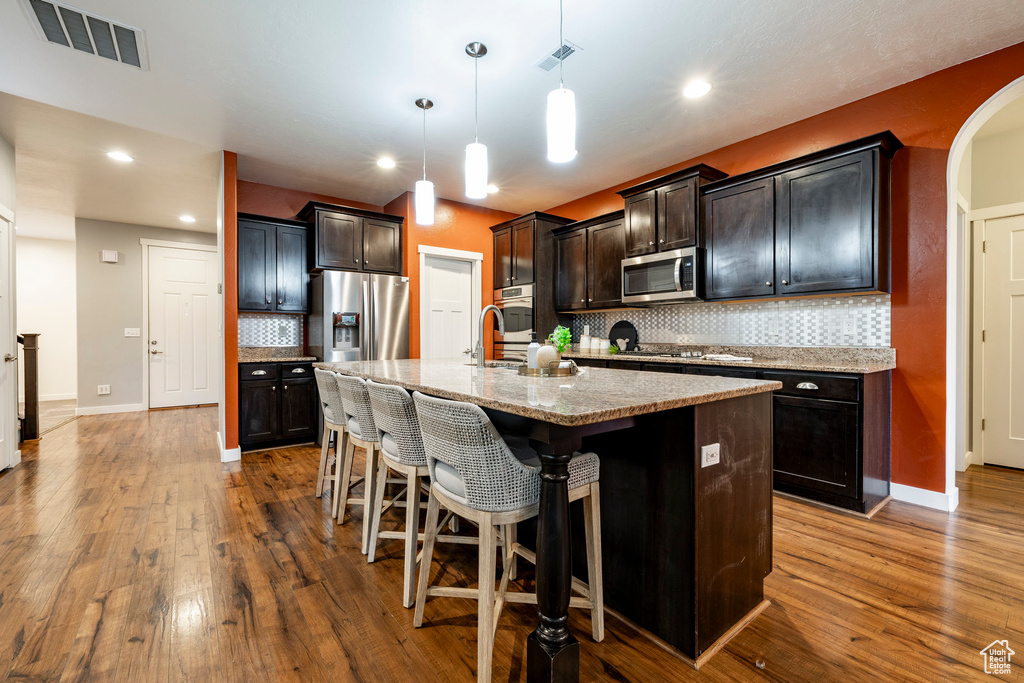 Kitchen with appliances with stainless steel finishes, dark wood-style flooring, a kitchen breakfast bar, backsplash, and baseboards