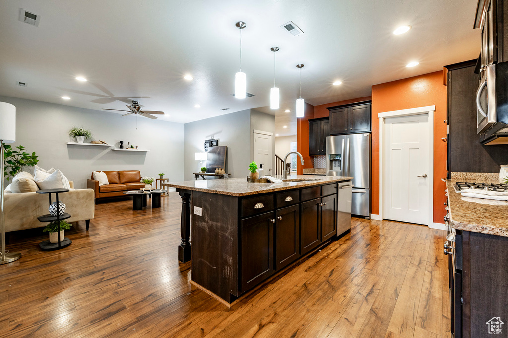 Kitchen featuring appliances with stainless steel finishes, a sink, open floor plan, a ceiling fan, and hardwood / wood-style flooring