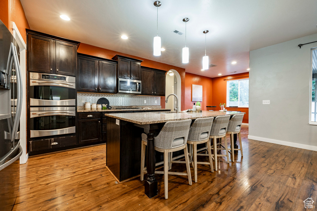 Kitchen featuring appliances with stainless steel finishes, a sink, backsplash, a breakfast bar, and light stone countertops