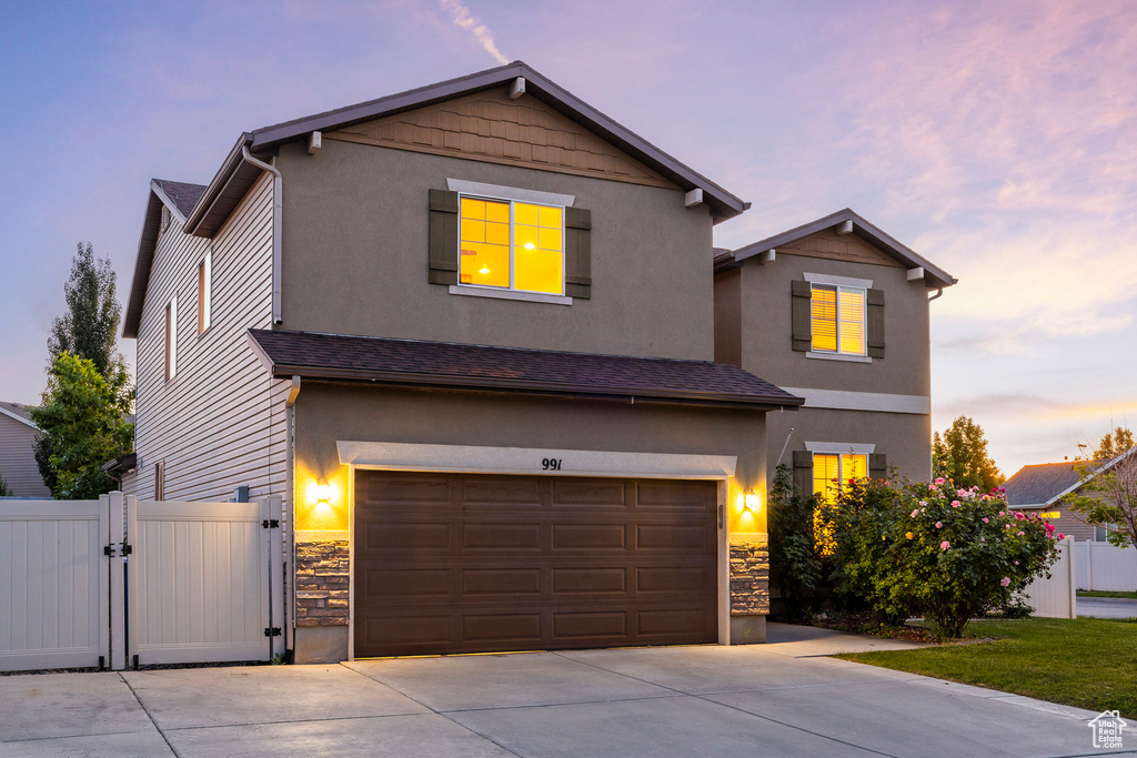 Traditional-style house with stone siding, concrete driveway, a gate, and a garage