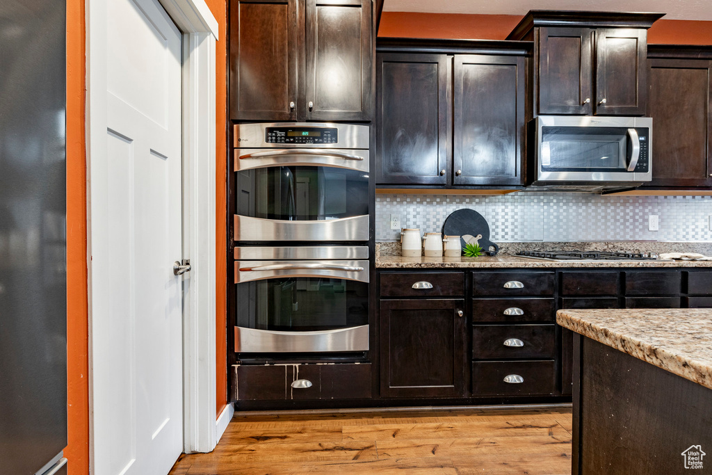 Kitchen featuring stainless steel appliances, light wood-style floors, backsplash, and light stone countertops