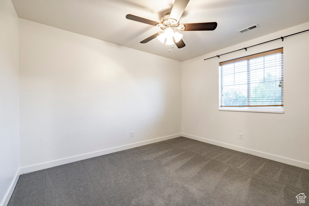 Spare room featuring dark colored carpet, baseboards, and ceiling fan