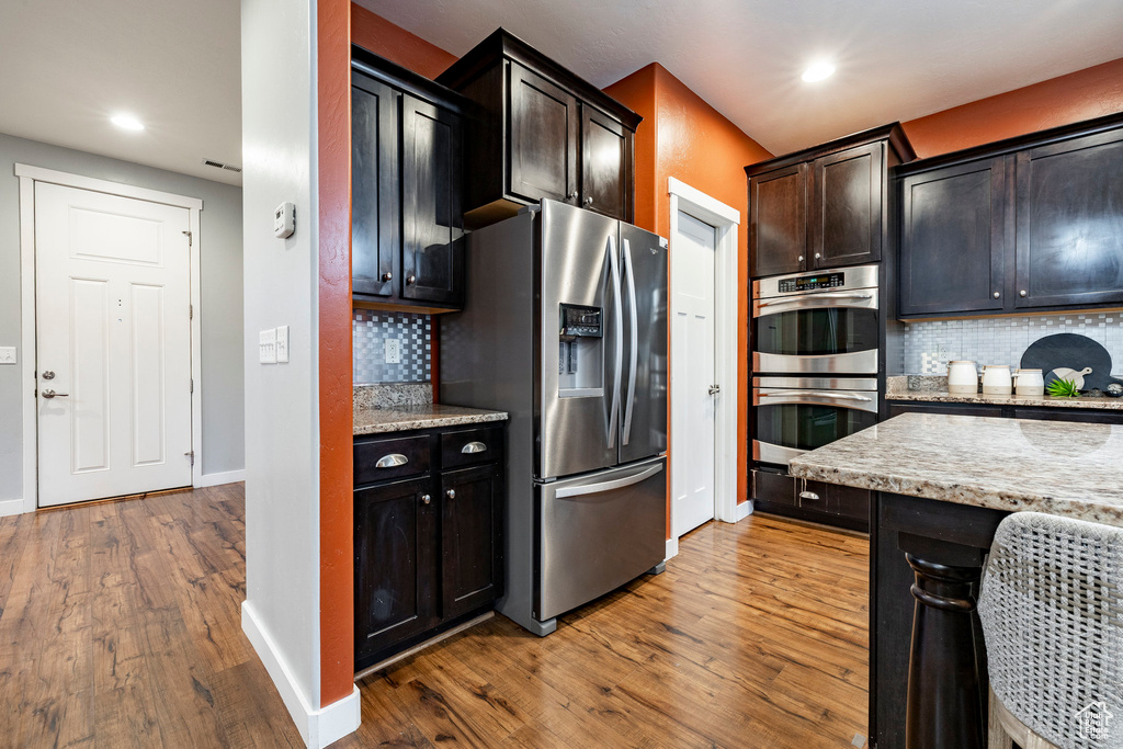Kitchen with appliances with stainless steel finishes, wood finished floors, tasteful backsplash, recessed lighting, and light stone counters