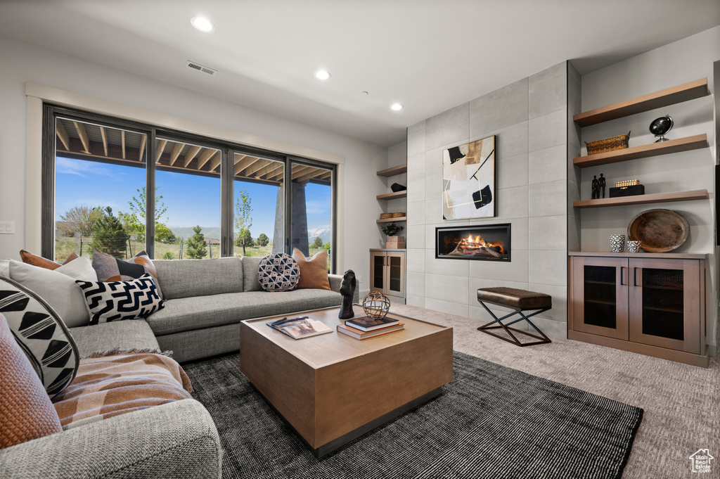 Living room with dark colored carpet, recessed lighting, and a tiled fireplace