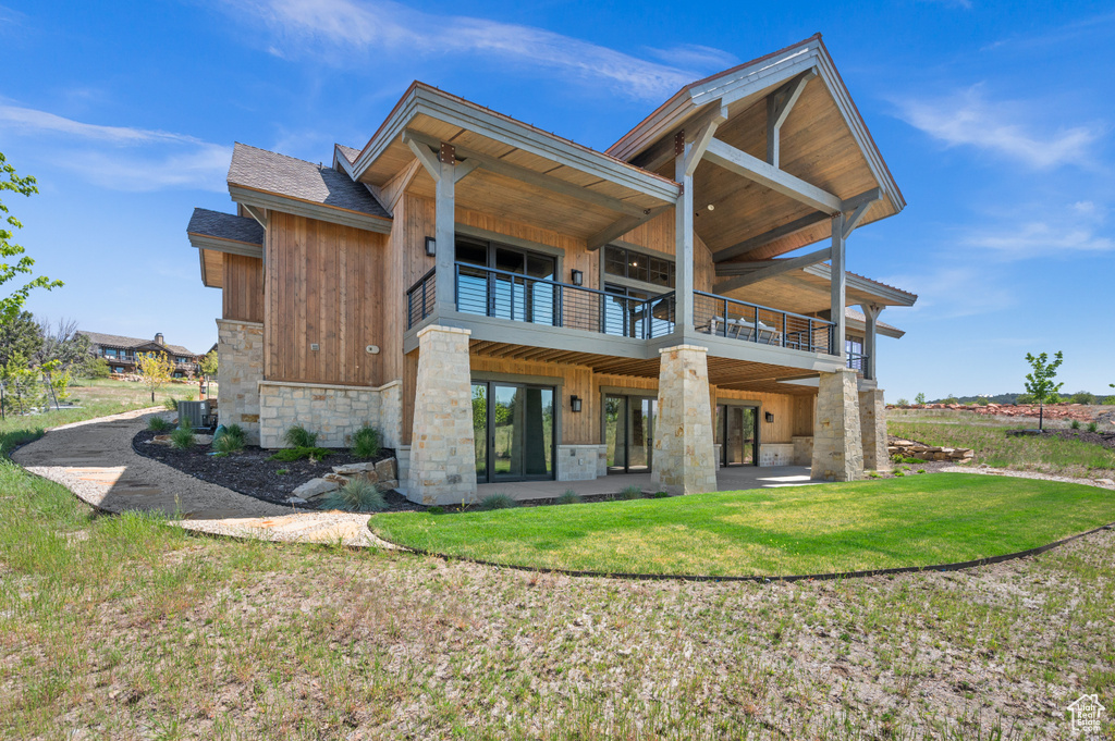 Rear view of property featuring stone siding, central air condition unit, a lawn, a patio area, and a balcony
