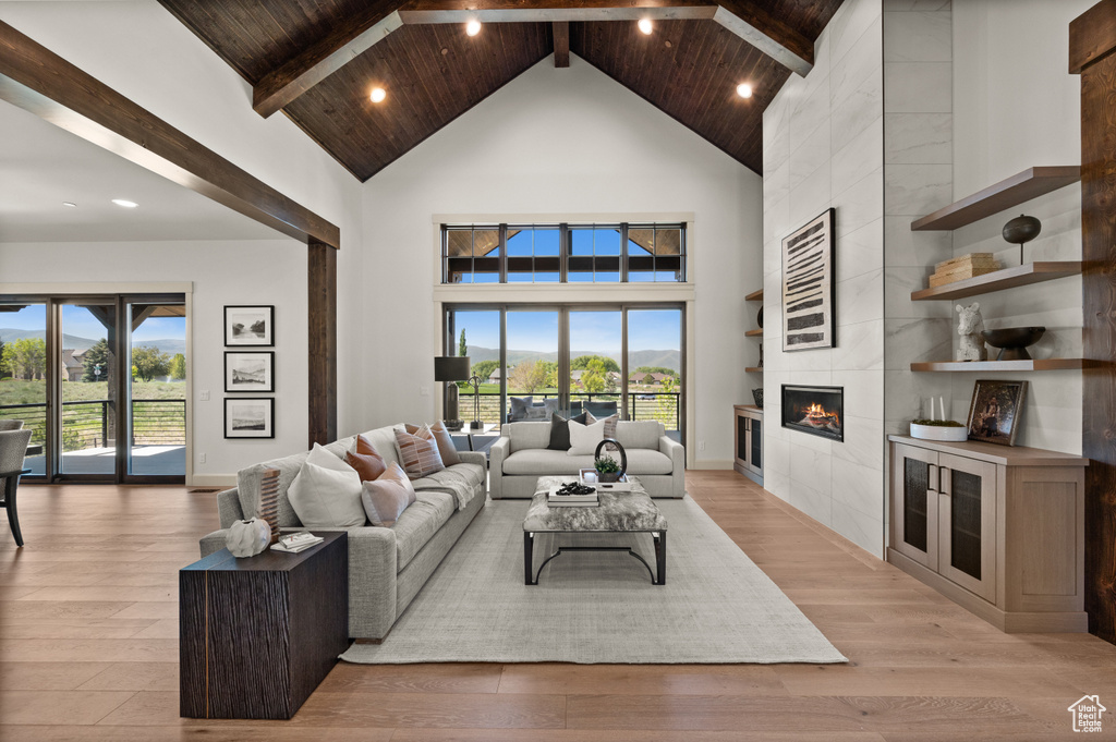 Living room featuring high vaulted ceiling, a fireplace, light wood-style floors, wooden ceiling with exposed beams, and recessed lighting