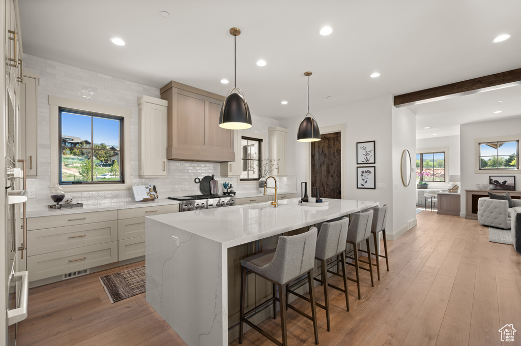 Kitchen featuring tasteful backsplash, an island with sink, a sink, light stone counters, and a breakfast bar