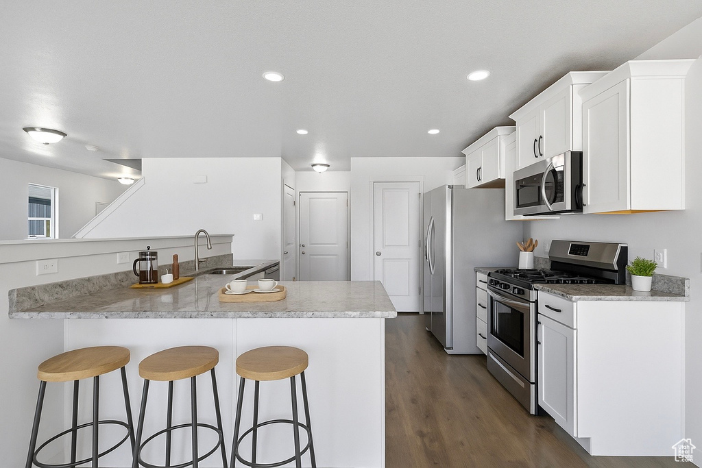 Kitchen with stainless steel appliances, a breakfast bar, white cabinetry, dark wood-style flooring, and recessed lighting