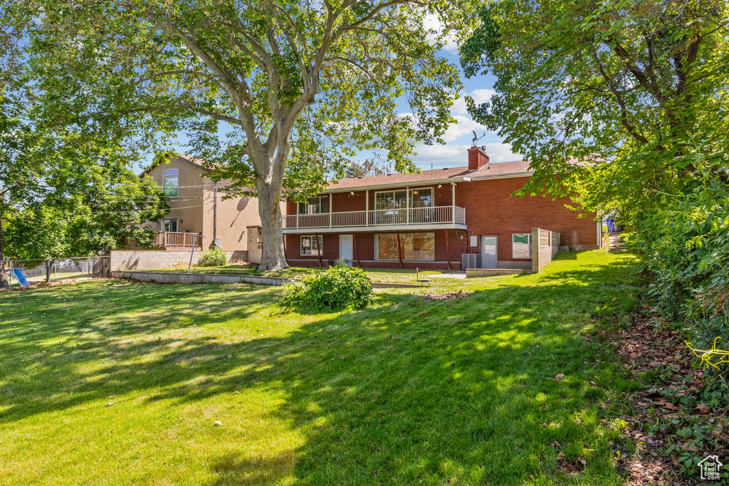 Rear view of house featuring brick siding, a chimney, and a balcony