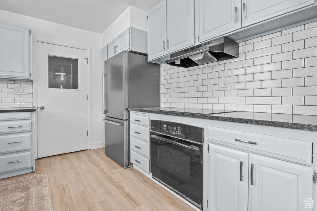 Kitchen featuring black appliances, under cabinet range hood, light wood-style flooring, tasteful backsplash, and white cabinetry