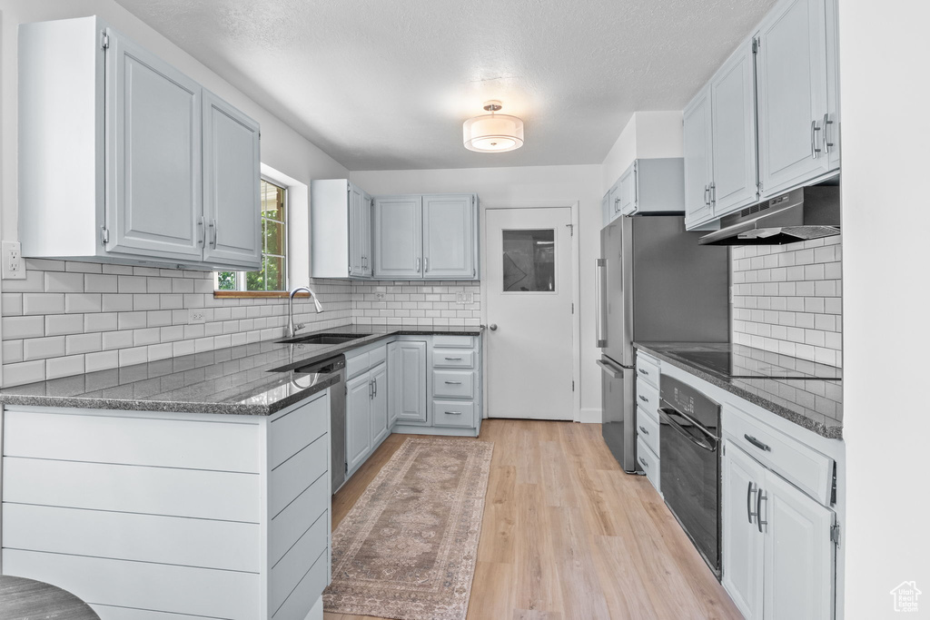 Kitchen featuring black oven, a sink, under cabinet range hood, light wood-style floors, and tasteful backsplash