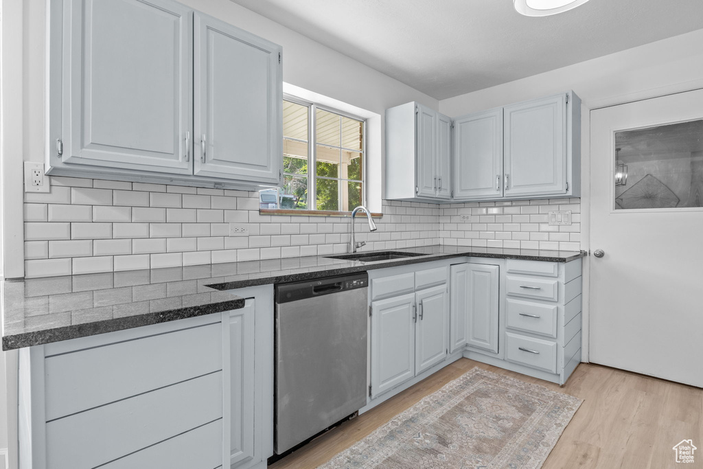 Kitchen with stainless steel dishwasher, a sink, light wood-type flooring, backsplash, and dark stone countertops