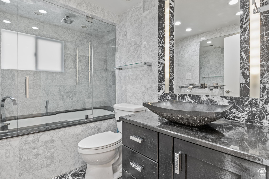 Bathroom featuring toilet, a combined bath / shower with rainfall shower, vanity, recessed lighting, and tile walls