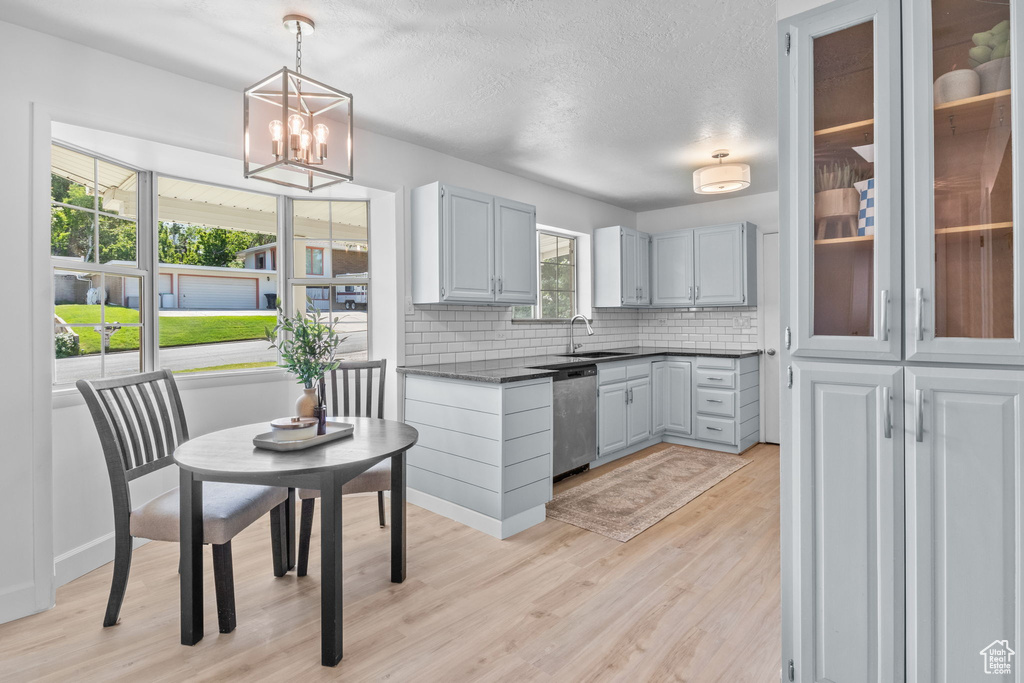 Kitchen with stainless steel dishwasher, dark countertops, backsplash, light wood-style flooring, and decorative light fixtures