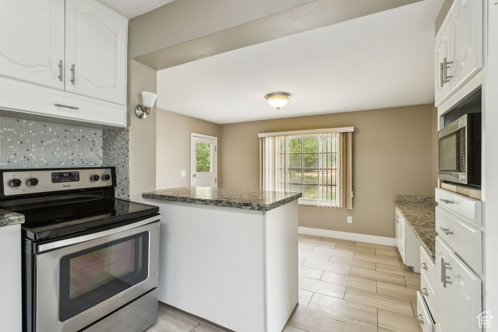 Kitchen with appliances with stainless steel finishes, tasteful backsplash, white cabinets, a peninsula, and dark stone countertops