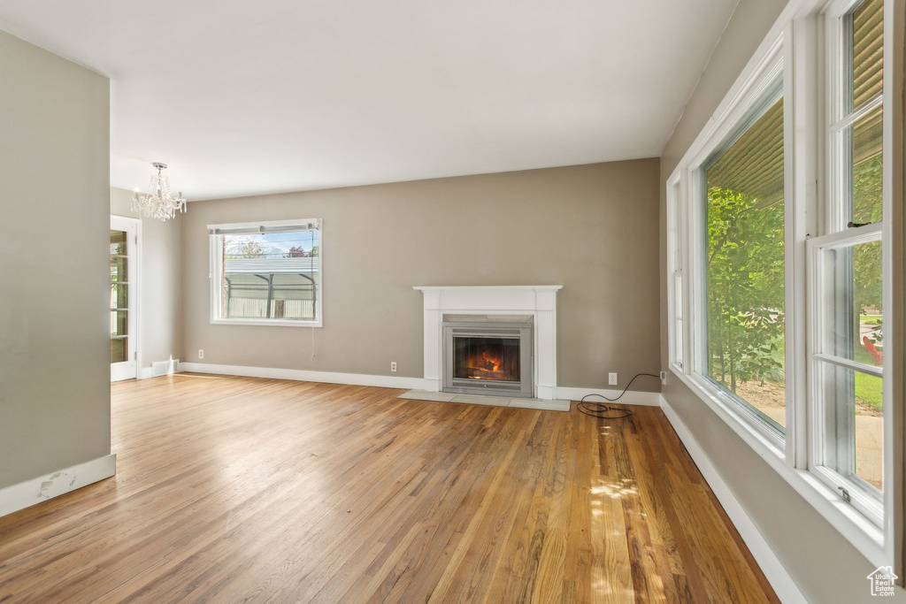 Unfurnished living room featuring light wood finished floors, a fireplace with flush hearth, a chandelier, and baseboards