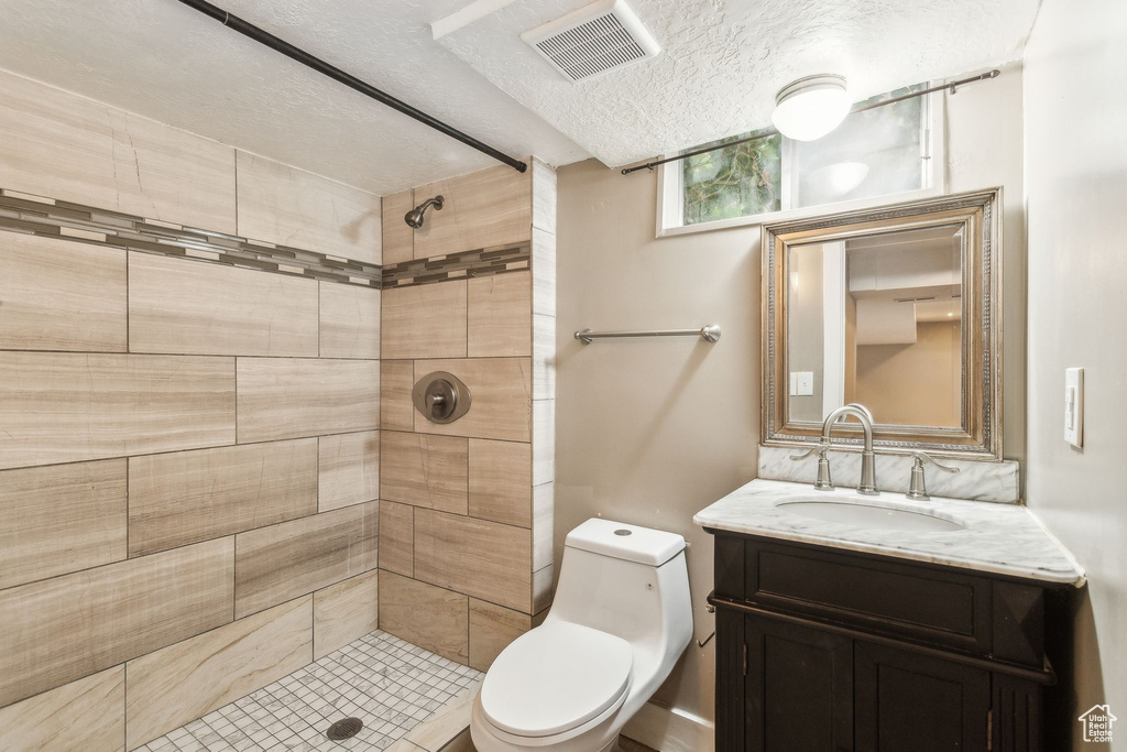Full bathroom featuring vanity, tiled shower, toilet, and a textured ceiling