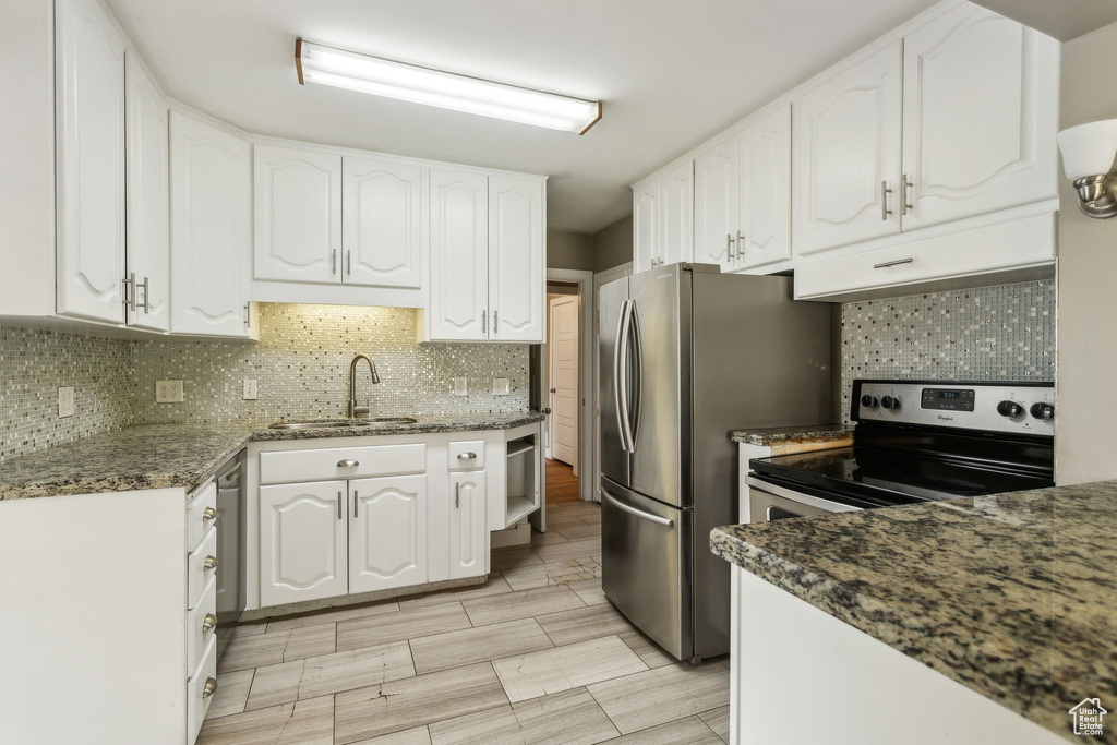 Kitchen featuring a sink, white cabinetry, backsplash, freestanding refrigerator, and dark stone countertops